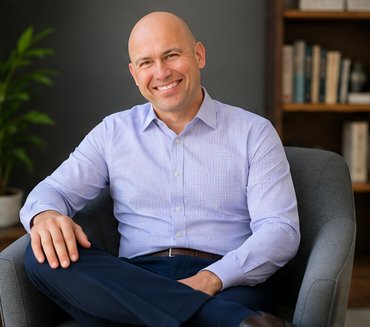 Robert Clark seated in an armchair in his low-lit counseling office, bookshelves behind him